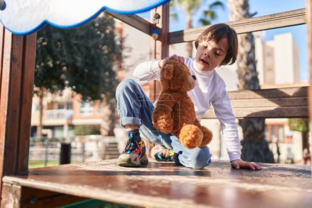 Foto de Síndrome de Down niño jugando con osito de peluche en la diapositiva en el parque - Imagen libre de derechos