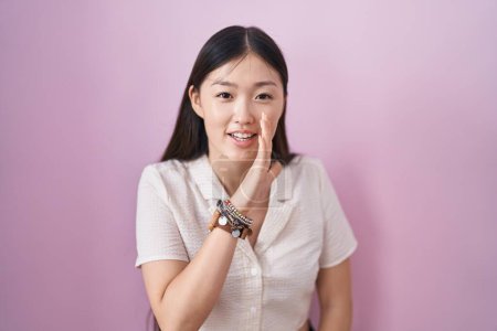 Téléchargez les photos : Chinese young woman standing over pink background hand on mouth telling secret rumor, whispering malicious talk conversation - en image libre de droit