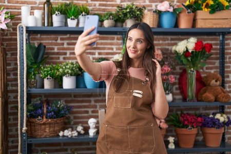 Téléchargez les photos : Young beautiful hispanic woman florist smiling confident make selfie by smartphone at flower shop - en image libre de droit