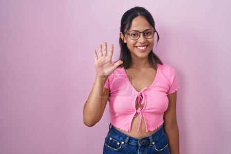 Téléchargez les photos : Hispanic young woman standing over pink background wearing glasses showing and pointing up with fingers number five while smiling confident and happy. - en image libre de droit