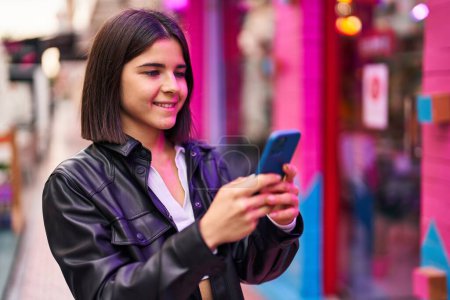 Téléchargez les photos : Jeune belle femme hispanique souriant confiant en utilisant smartphone à la rue - en image libre de droit