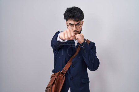 Foto de Hispanic man with beard wearing business clothes punching fist to fight, aggressive and angry attack, threat and violence - Imagen libre de derechos