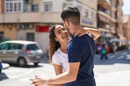 Foto de Joven pareja hispana sonriendo confiada abrazándose y bailando en la calle - Imagen libre de derechos