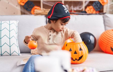 Téléchargez les photos : Adorable garçon hispanique ayant fête d'Halloween tenant panier de citrouille à la maison - en image libre de droit