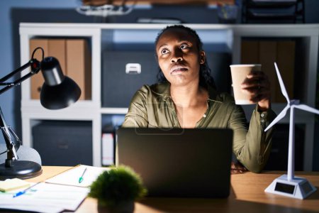 Téléchargez les photos : Femme africaine travaillant à l'aide d'un ordinateur portable la nuit à la recherche somnolent et fatigué, épuisé par la fatigue et la gueule de bois, les yeux paresseux le matin. - en image libre de droit