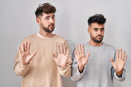 Photo for Young homosexual couple standing over white background moving away hands palms showing refusal and denial with afraid and disgusting expression. stop and forbidden. - Royalty Free Image