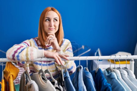 Photo for Young woman searching clothes on clothing rack serious face thinking about question with hand on chin, thoughtful about confusing idea - Royalty Free Image