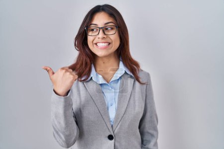 Photo for Hispanic young business woman wearing glasses smiling with happy face looking and pointing to the side with thumb up. - Royalty Free Image