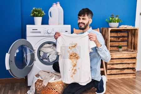 Photo for Young hispanic man with beard holding clean white t shirt and t shirt with dirty stain winking looking at the camera with sexy expression, cheerful and happy face. - Royalty Free Image