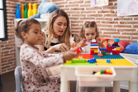 Foto de Profesor con niñas jugando con bloques de construcción sentado en la mesa en el jardín de infantes - Imagen libre de derechos