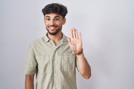 Téléchargez les photos : Arab man with beard standing over white background waiving saying hello happy and smiling, friendly welcome gesture - en image libre de droit