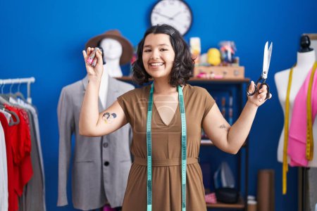Photo for Young woman tailor smiling confident holding scissors and thread at sewing studio - Royalty Free Image