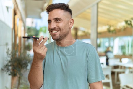 Téléchargez les photos : Jeune homme hispanique souriant confiant parler sur le smartphone à la terrasse du café - en image libre de droit