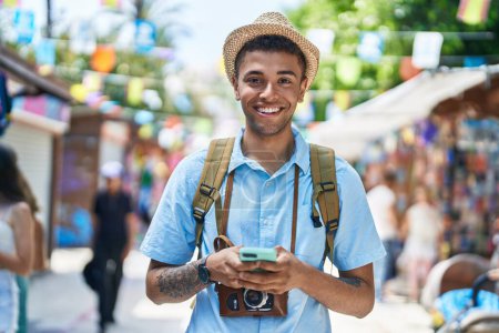 Téléchargez les photos : Africain américain touriste souriant confiant en utilisant smartphone au marché de la rue - en image libre de droit