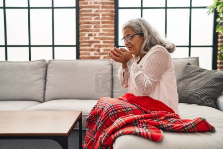 Foto de Mujer de mediana edad bebiendo café sentado en el sofá en casa - Imagen libre de derechos