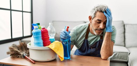 Foto de Middle age grey-haired man tired cleaning table at home - Imagen libre de derechos