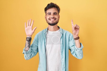 Téléchargez les photos : Young hispanic man with tattoos standing over yellow background showing and pointing up with fingers number six while smiling confident and happy. - en image libre de droit