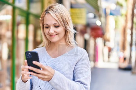Photo for Young blonde woman smiling confident using smartphone at street - Royalty Free Image