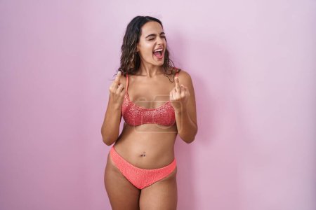 Téléchargez les photos : Young hispanic woman wearing lingerie over pink background showing middle finger doing fuck you bad expression, provocation and rude attitude. screaming excited - en image libre de droit