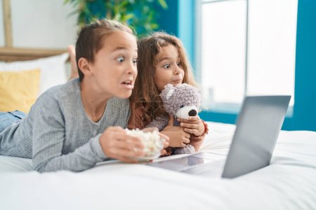 Photo for Two kids watching movie on laptop lying on bed with scary expression at bedroom - Royalty Free Image