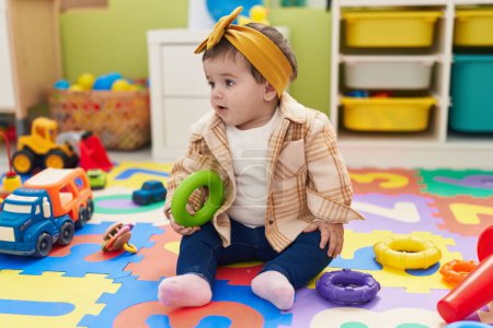 Foto de Adorable niño rubio sentado en el suelo sosteniendo el juguete del aro en el jardín de infantes - Imagen libre de derechos