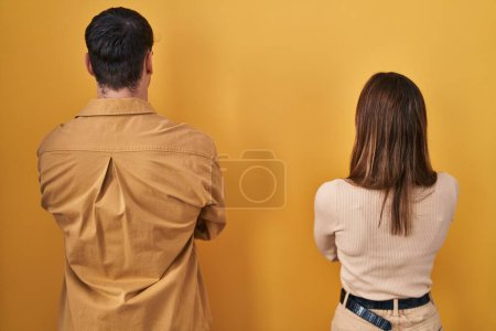 Foto de Young hispanic couple standing over yellow background standing backwards looking away with crossed arms - Imagen libre de derechos