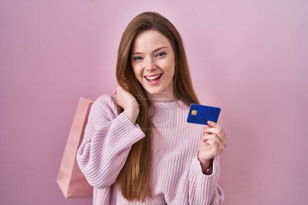 Photo for Young caucasian woman holding shopping bag and credit card smiling and laughing hard out loud because funny crazy joke. - Royalty Free Image