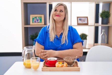 Photo for Caucasian plus size woman eating breakfast at home smiling looking to the side and staring away thinking. - Royalty Free Image