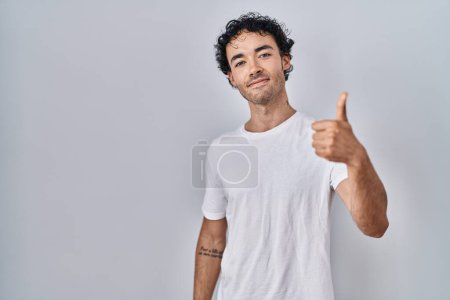 Téléchargez les photos : Hispanic man standing over isolated background doing happy thumbs up gesture with hand. approving expression looking at the camera showing success. - en image libre de droit