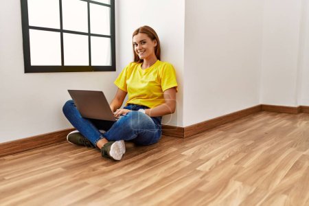 Photo for Young woman using laptop sitting on floor at empty room - Royalty Free Image