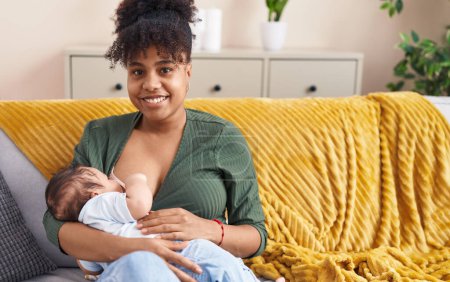 Photo for Mother and son sitting on sofa breastfeeding at home - Royalty Free Image
