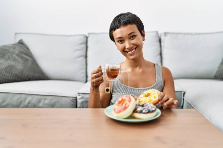 Foto de Joven mujer hispana sonriendo confiada desayunando en casa - Imagen libre de derechos