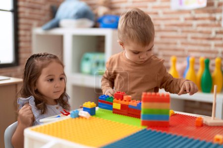 Téléchargez les photos : Adorable fille et garçon jouant avec des blocs de construction assis sur la table à la maternelle - en image libre de droit