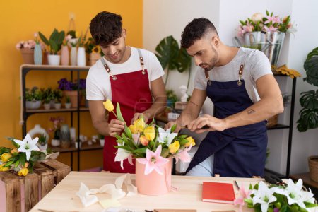 Téléchargez les photos : Two hispanic men florists smiling confident make bouquet of flowers at flower shop - en image libre de droit