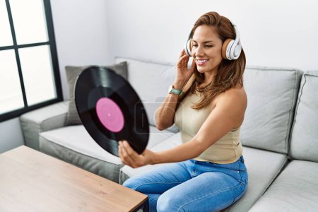 Photo for Young latin woman listening to music holding vinyl disc at home - Royalty Free Image