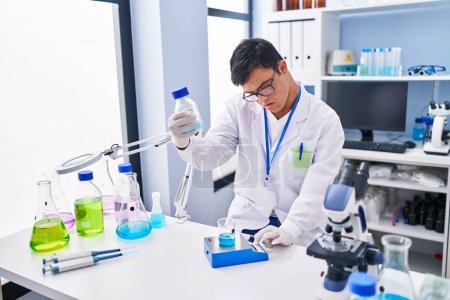 Téléchargez les photos : Homme trisomique portant un uniforme scientifique mesurant le liquide en laboratoire - en image libre de droit
