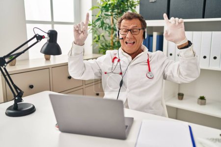 Téléchargez les photos : Senior doctor man working on online appointment smiling amazed and surprised and pointing up with fingers and raised arms. - en image libre de droit