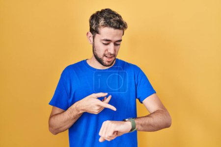 Téléchargez les photos : Hispanic man with beard standing over yellow background in hurry pointing to watch time, impatience, upset and angry for deadline delay - en image libre de droit