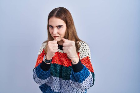 Photo for Young hispanic girl standing over blue background ready to fight with fist defense gesture, angry and upset face, afraid of problem - Royalty Free Image