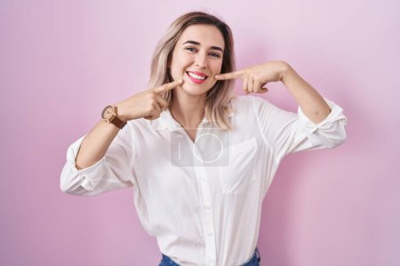 Téléchargez les photos : Jeune belle femme debout sur fond rose souriant gai montrant et pointant avec les doigts dents et la bouche. concept de santé dentaire. - en image libre de droit