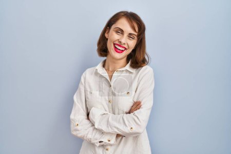 Foto de Young beautiful woman standing casual over blue background happy face smiling with crossed arms looking at the camera. positive person. - Imagen libre de derechos