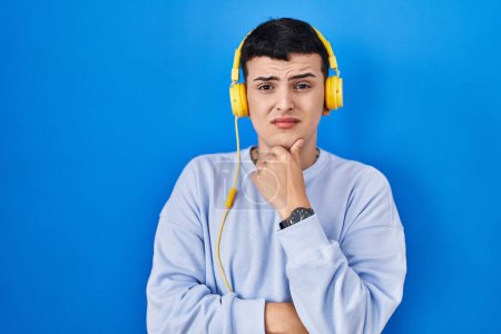 Photo for Non binary person listening to music using headphones thinking worried about a question, concerned and nervous with hand on chin - Royalty Free Image