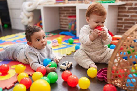 Téléchargez les photos : Deux adorables bébés jouant avec des couilles assises sur le sol à la maternelle - en image libre de droit