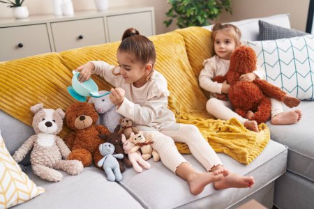 Photo for Two kids playing with dolls sitting on sofa at home - Royalty Free Image