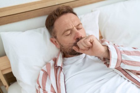 Téléchargez les photos : Middle age man lying on bed coughing at bedroom - en image libre de droit