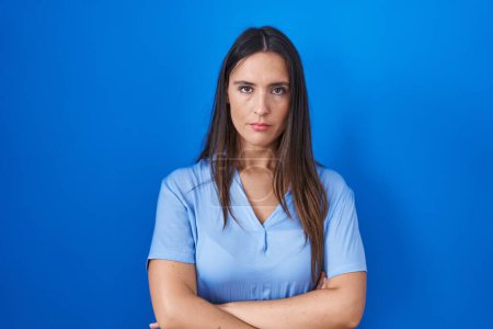 Photo for Young brunette woman standing over blue background skeptic and nervous, disapproving expression on face with crossed arms. negative person. - Royalty Free Image