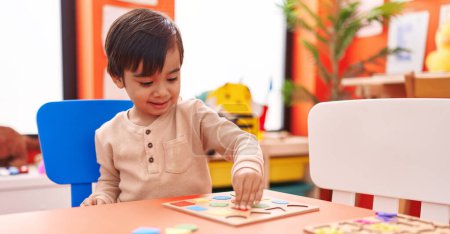 Photo for Adorable hispanic boy playing with maths puzzle game sitting on table at kindergarten - Royalty Free Image