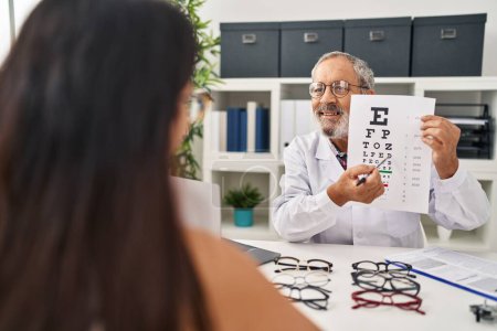 Photo for Senior grey-haired man optician doing snellen eye test to patient at clinic - Royalty Free Image