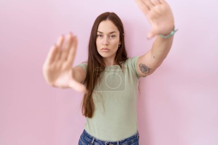Foto de Beautiful brunette woman standing over pink background doing frame using hands palms and fingers, camera perspective - Imagen libre de derechos