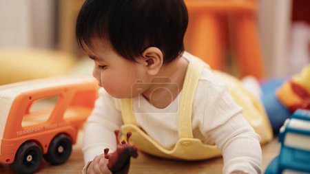 Photo for Adorable hispanic baby playing with cars toy lying on floor at kindergarten - Royalty Free Image